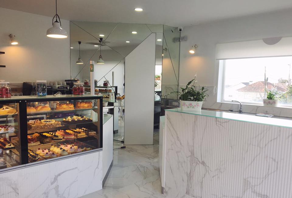 Sala clara da pastelaria, com balcão de mármore e vitrina de bolos